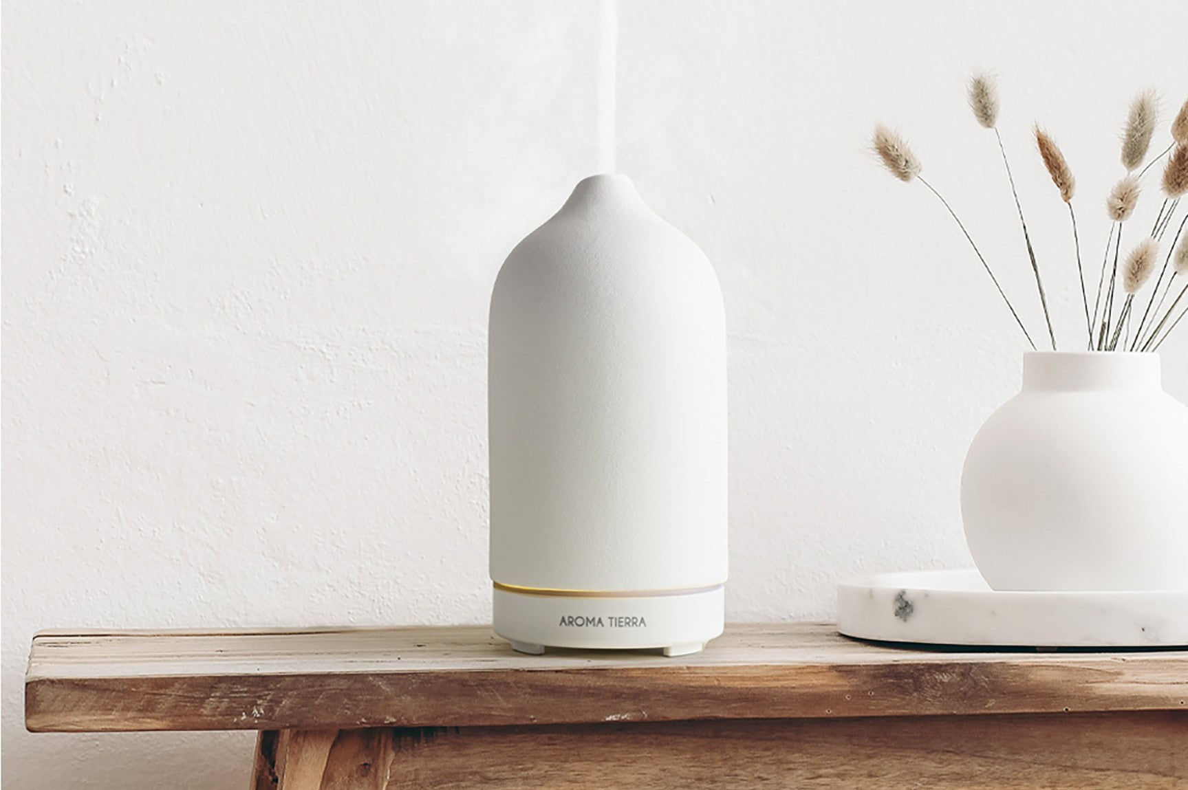 Minimalist ceramic essential oil diffuser emitting mist on a wooden shelf, promoting natural aromatherapy and non-toxic home fragrance.