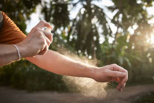 Person applying insect repellent on bare skin outdoors.