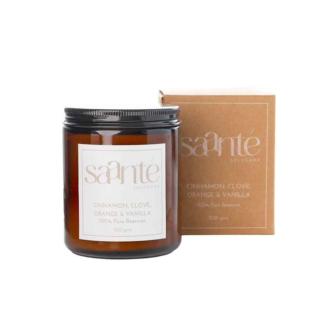 Saanté Self-Care cinnamon, clove, orange and vanilla beeswax candle in an amber jar, displayed next to its kraft packaging.