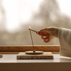 Hand lighting an incense stick on a small stone platform with a blurred background